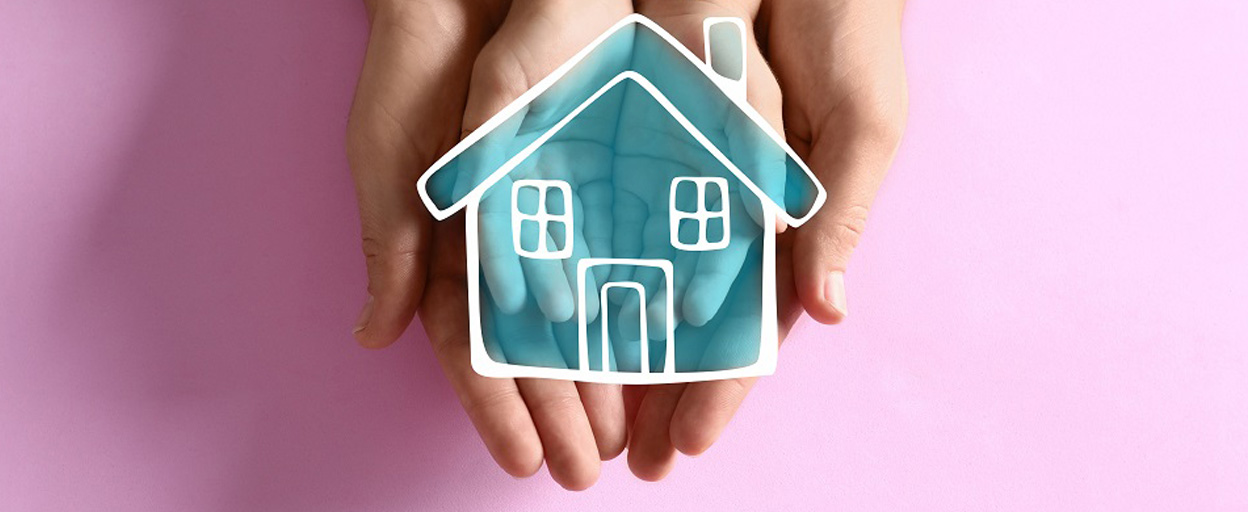 Two hands coming together to hold a drawing of a blue house with a pink background 