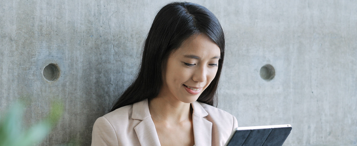 Woman with black hair looking at tablet standing against wall