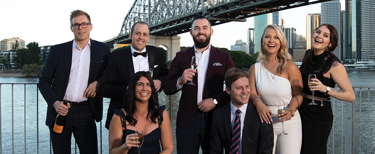 Men and women dressed formally in front of Story Bridge