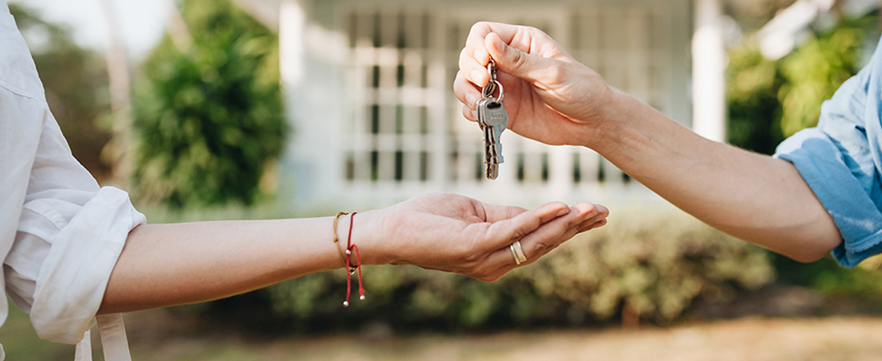 Man handing keys to woman in front of house