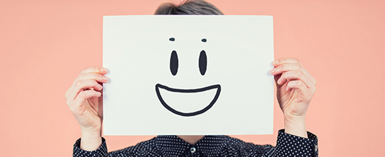 Woman holding paper up with smiley face with peach background