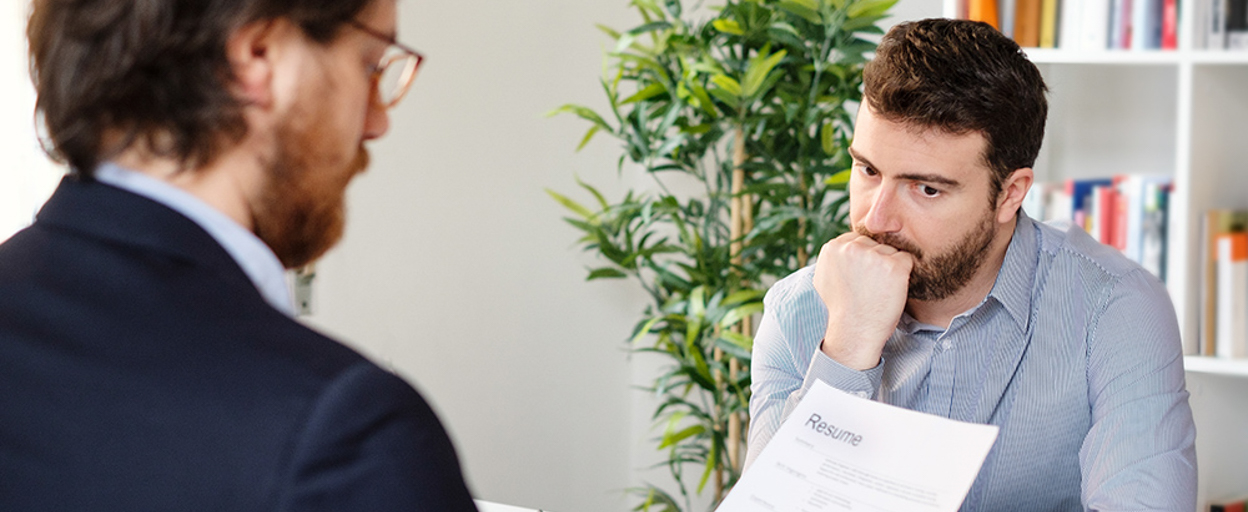 Pensive man looking at man across desk with paperwork