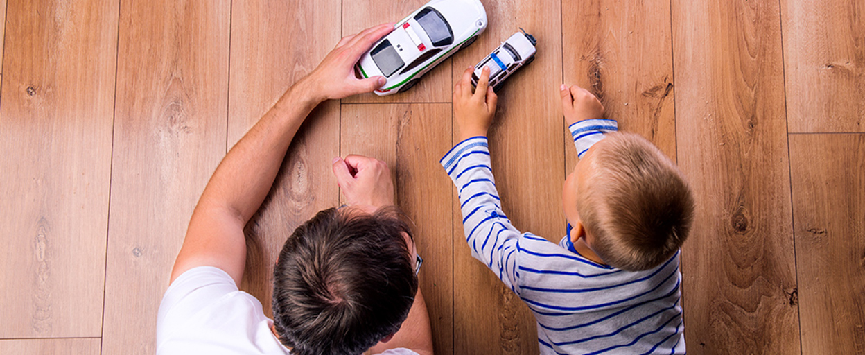 Man and boy on wood floor playing with toy cars