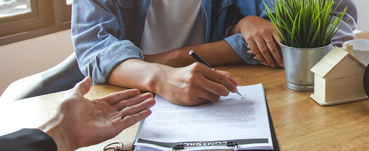Man signing paperwork on table with plant