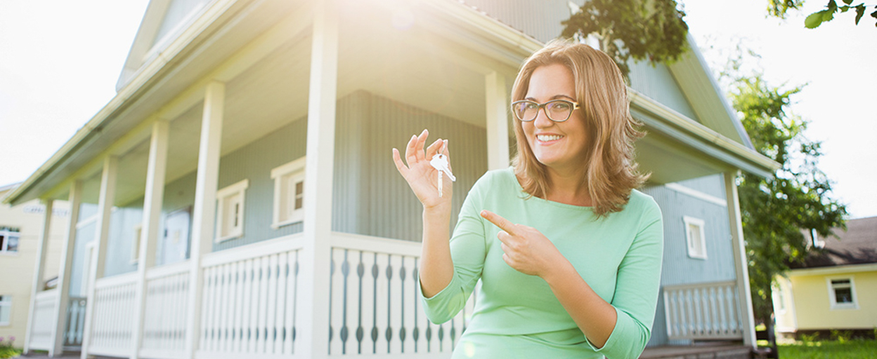 Woman holding keys smiling in front of house