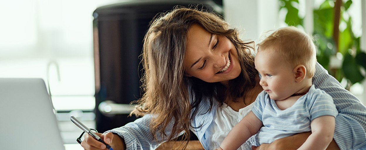 Woman smiling at baby on lap at table with computer