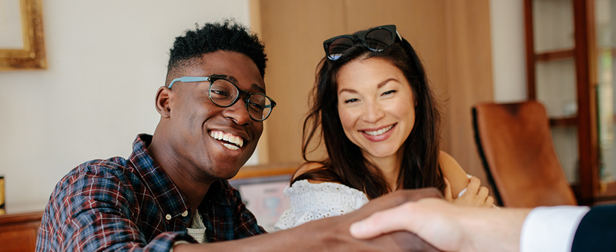Couple smiling whilst man shakes hands with other man