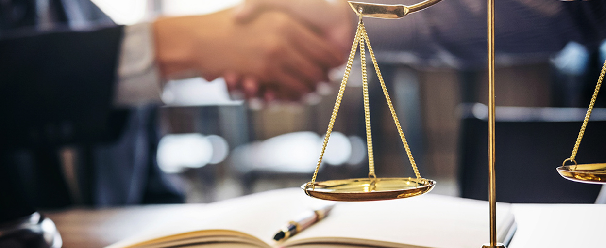 2 men shaking hands behind set of scales and notebook