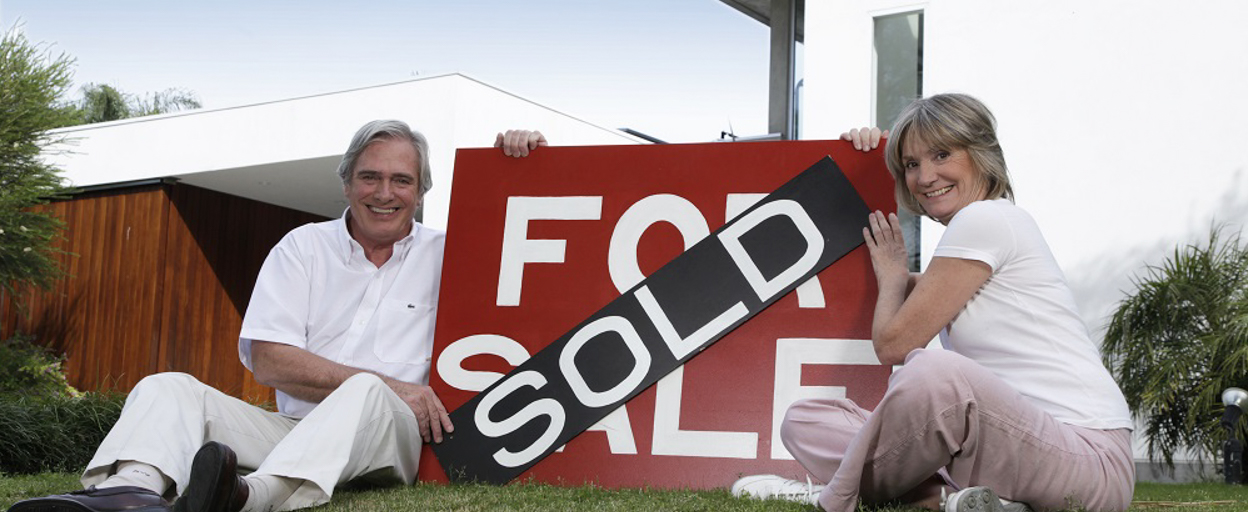 Seniors couple with sold sign outside their home