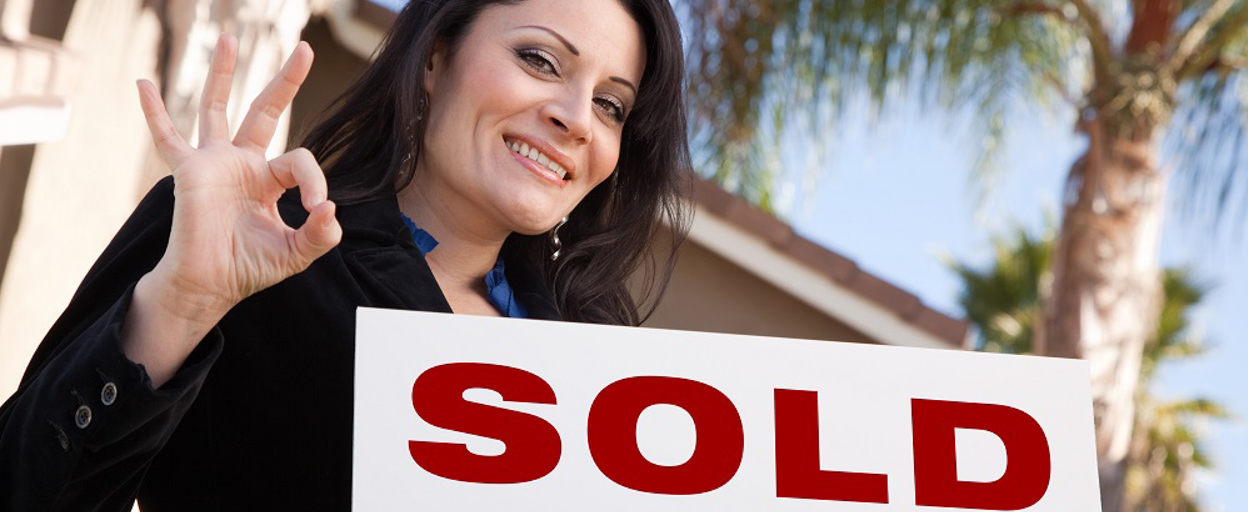 Woman smiling with SOLD sign in front of house