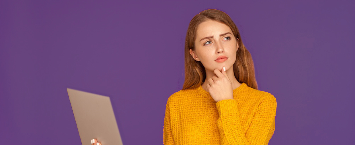 Pensive woman in yellow jumper with laptop in front of purple background