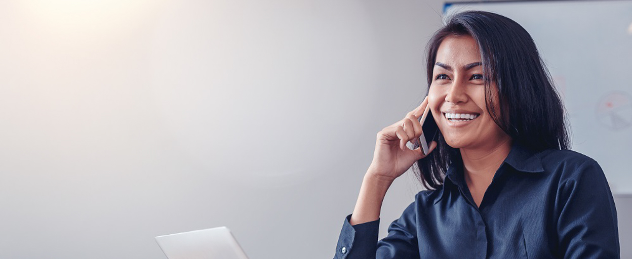 Woman smiling on the phone with laptop and grey background
