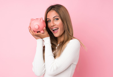 Female smiling while holding up a pink piggy bank with a pink background