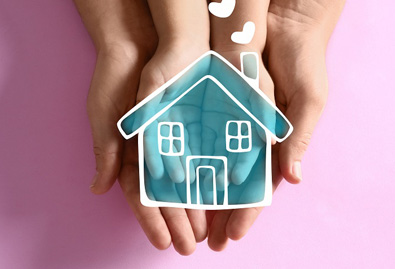 Two hands coming together to hold a drawing of a blue house with a pink background 