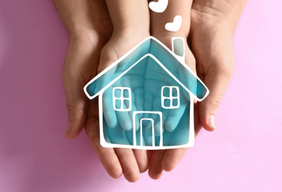 Two hands coming together to hold a drawing of a blue house with a pink background