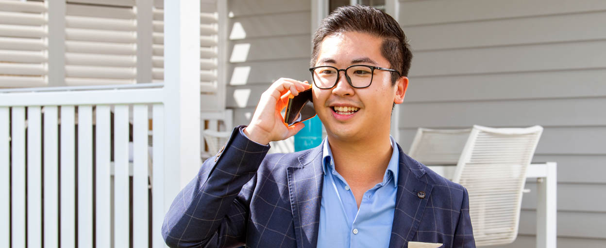 Male real estate agent on the phone smiling outside of a residential house